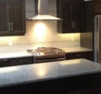 Finished kitchen by Gold Wing Construction with dark-stained cabinetry, a granite-topped island, tile backsplash and stainless range hood